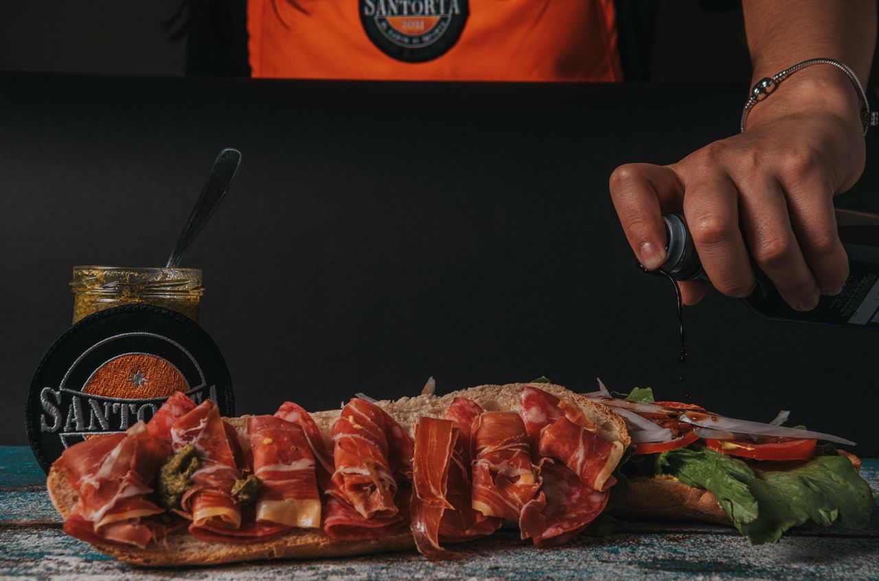 Close-up of a gourmet sandwich being prepared with fresh ingredients and sauces.
